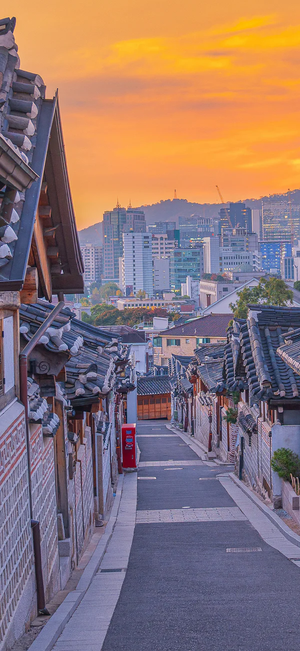 Sunset over Bukchon Hanok Village in Seoul, South Korea, with the city skyline in the background