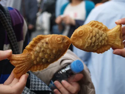 Two people are holding up taiyaki cakes so the fish look like they're kissing