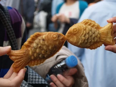 Two people are holding up taiyaki cakes so the fish look like they're kissing