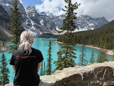 A woman in a TourCompass T-shirt gazes out across the water at Lake Louise in Canada