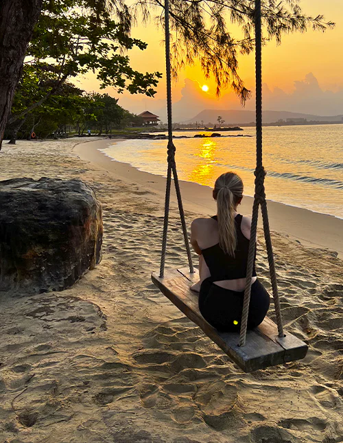 A person sits on a swing on a beach, enjoying the sunset