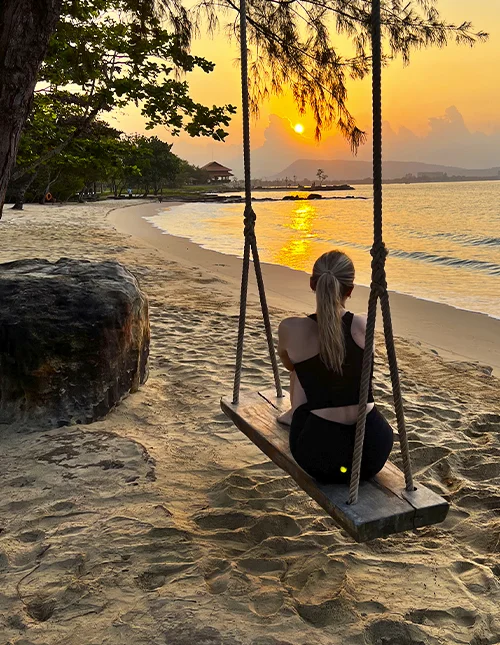 A person sits on a swing on a beach, enjoying the sunset