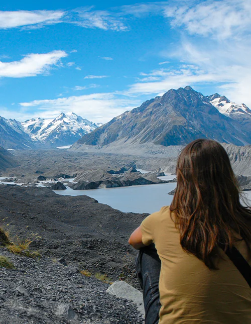 A person admiring the snow-capped mountains and the beautiful glacial lake in Aoraki/Mount Cook National Park, New Zealand