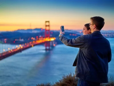 Man and woman photographing the Golden Gate Bridge at sunset