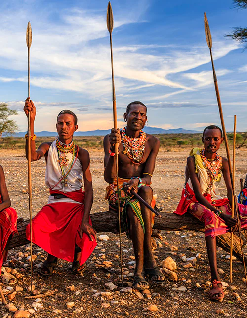 A group of Maasai people sit on the savannah, holding spears in their hands