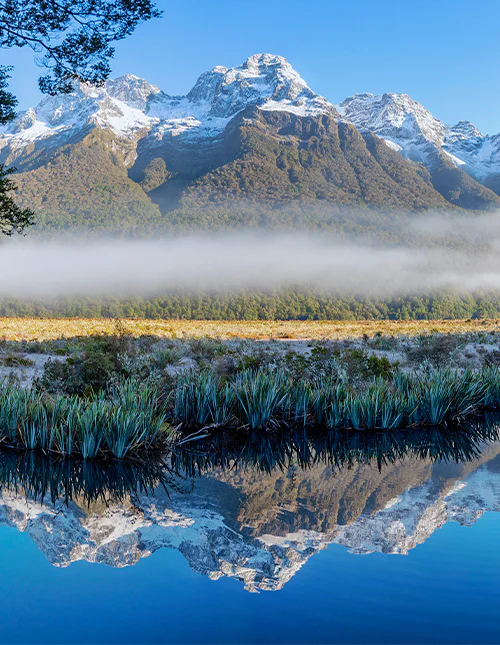 Mirror Lake, low lying fog and snow colored peaks on a clear winter day in Milford Sound, New Zealand