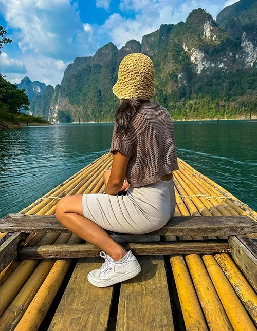 Woman gliding across a Thai lake on a bamboo raft, framed by dramatic limestone mountains.