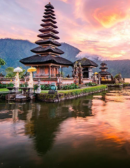 Beautiful temple by a lake at sunset, with mountains reflected in the water.