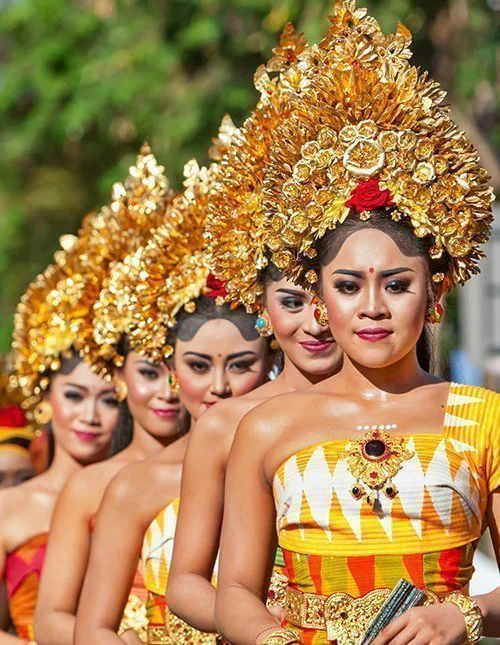 Traditional Balinese dancers in colourful costumes and golden headdresses in a procession.