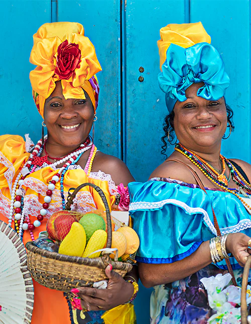 Two women in colourful dresses and headscarves in front of a blue door