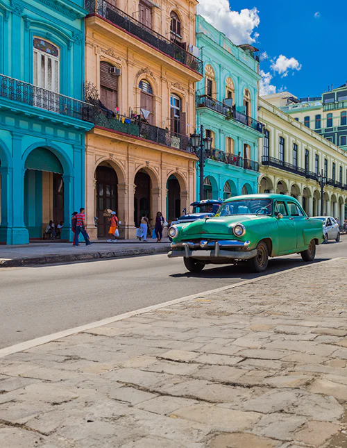 Colourful colonial buildings in Cuba and a classic green car on a sunny city street.