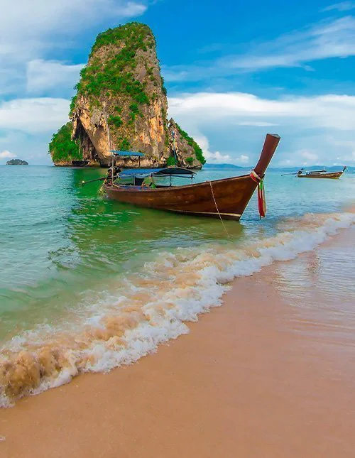 Longtail boat by a tropical beach and a limestone cliff in crystal-clear water